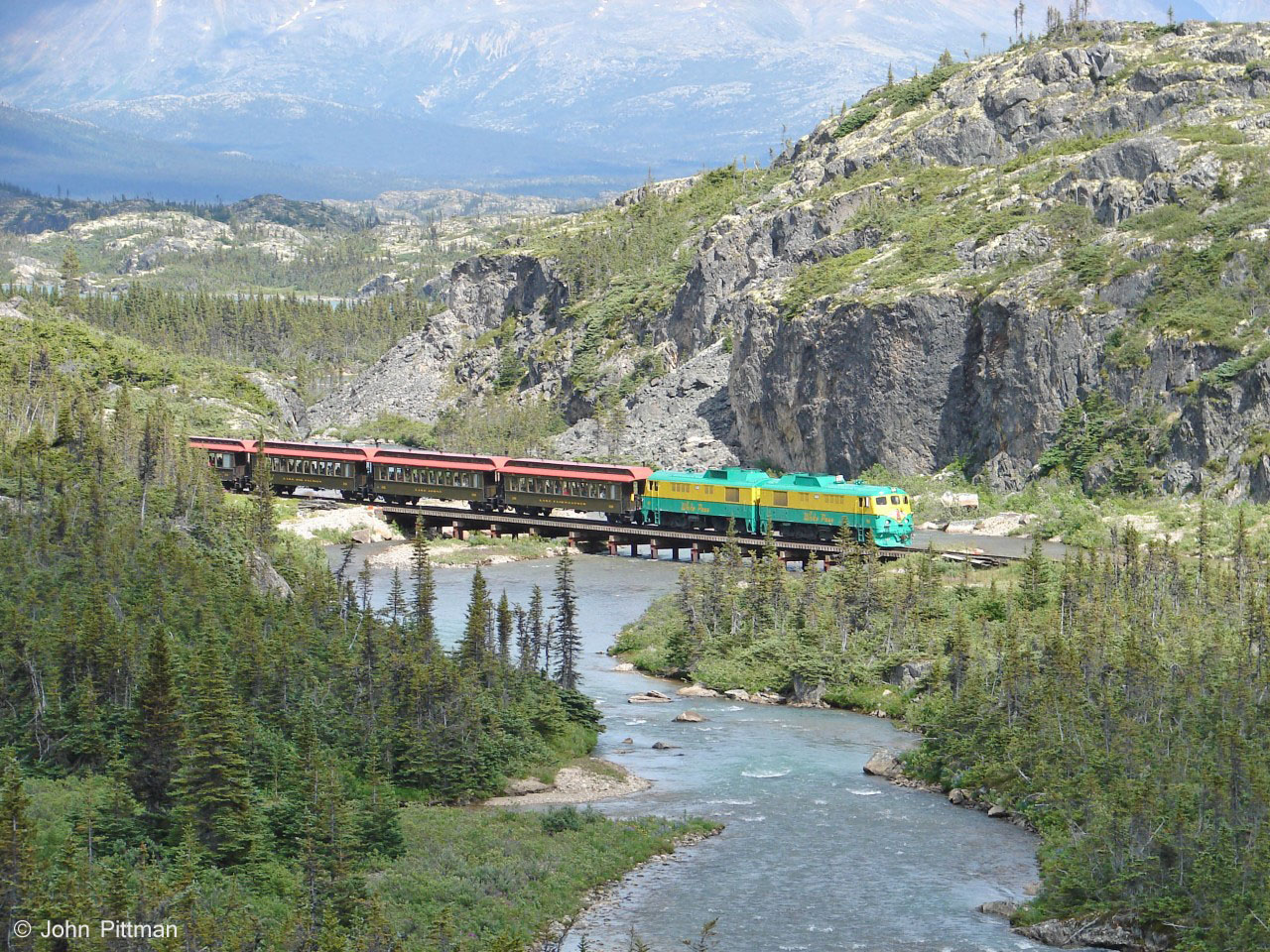 Approximately a mile south of Fraser depot (also south of the turning loop), the WP&YR crosses the river which carries water from Summit Lake to Bernard Lake.  I noted this scenic spot as I passed it driving north on the Klondike Highway some hours earlier, and hurried here to intercept the train I saw departing Fraser BC. 
The highway, river, and railway run parallel for a short distance south of here before diverging.  For most of its route, the White Pass & Yukon Railway is far from the nearest road, often the far side of a river, lake, or rugged terrain.  
If the  weather cooperates, this is a great place to photograph a train.  But it is Pacific coastal mountain territory so cloud and rain happen.   
Anyone interested in learning more about "North America's busiest tourist railroad" can find the May 2006 Trains Magazine article online at:  http://wpyr.com/railfans/trains-magazine/   
Another magazine article on the WP&YR official site is:   http://wpyr.com/railfans/railways-illustrated/
The WP&YR is currently owned by TWC Enterprises Limited of King City Ontario.