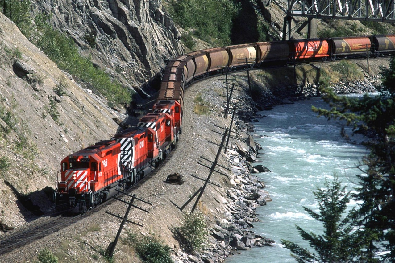 A westbound grain train passes under the now-removed Trans Canada Highway bridge just east of Glenogle Siding. Since this time a new alignment of the TCH takes traffic over a very high bridge over this part of Kicking Horse Canyon.