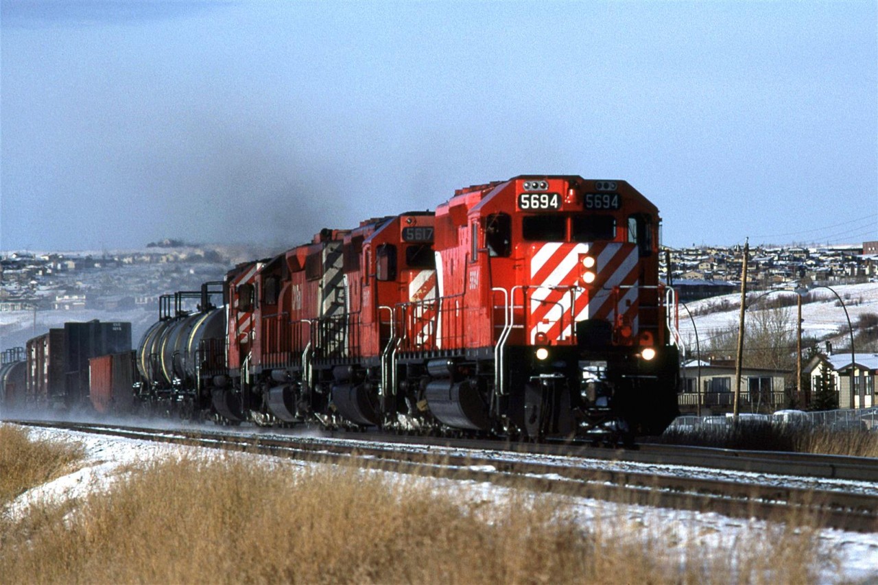 An eatbound manifest barrels through Brickburn in west Calgary. The first 3 cars appear to be used for liquid sulphur transport.
