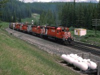 This westbound grain train is very close to the high point of Kicking Horse Pass. The propane heaters are for the crossovers for a grade separation between this point and Lake Louise. The train is on the new gentler alignment, while the old line is obscured by the train.