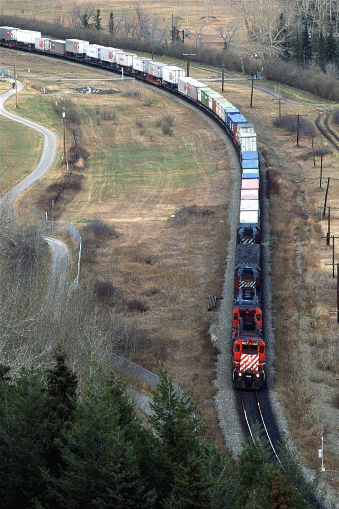 An eastbound relatively hot train usually came into town about the same time as VIA's #2. Today, it is preceding the passenger train. It is through Brickburn Siding, and is now in the center of Edworthy Park.
I believe that the fencing was fairly new at the time, and I suspect that there is lots more these days.