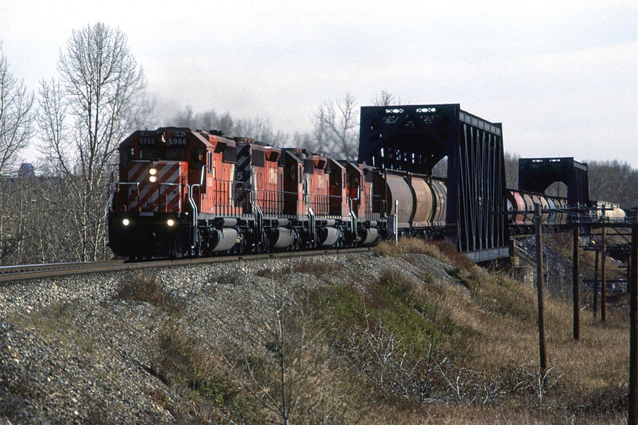 A westbound manifest train crossed the two bridges used to span the Bow River in west Calgary. In about another kilometer, the train will be at the east switch for Kieth Yard, a facility built to handle bulk commodity trains.