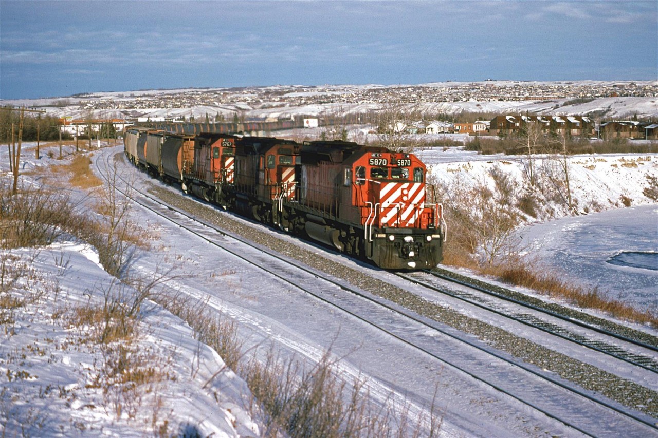 It is cold, but sunny in Calgary on this Mid-December day. There appears to be no warming chinook winds. The folks on the eastbound CP grain train probably think that I am nuts.
This is Brickburn siding and beyond is a frozen Bow River.