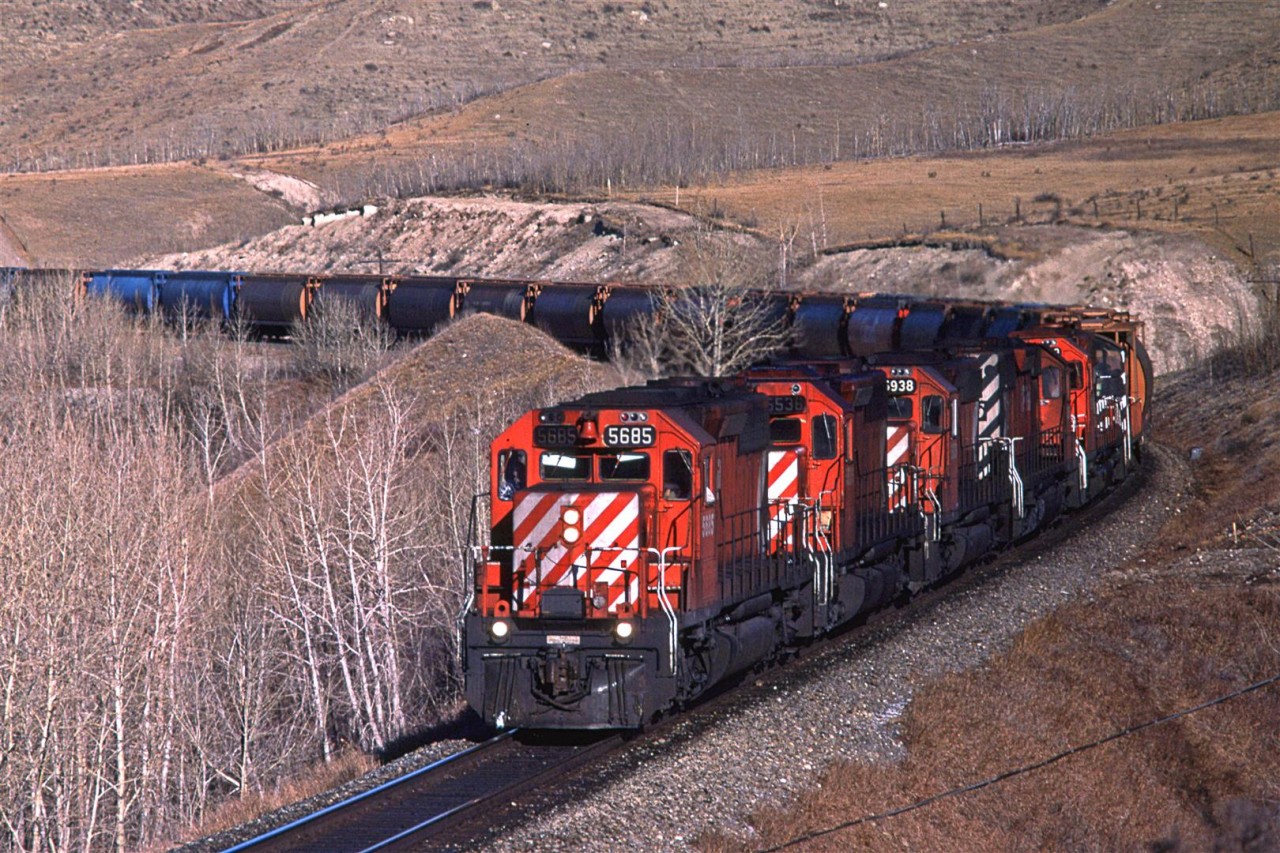 At about 1100 hrs on the first day of February, 1986, this eastbound grain train curves around the bluffs that mark the north side of the Bow River Valley between Cochrane and Calgary.