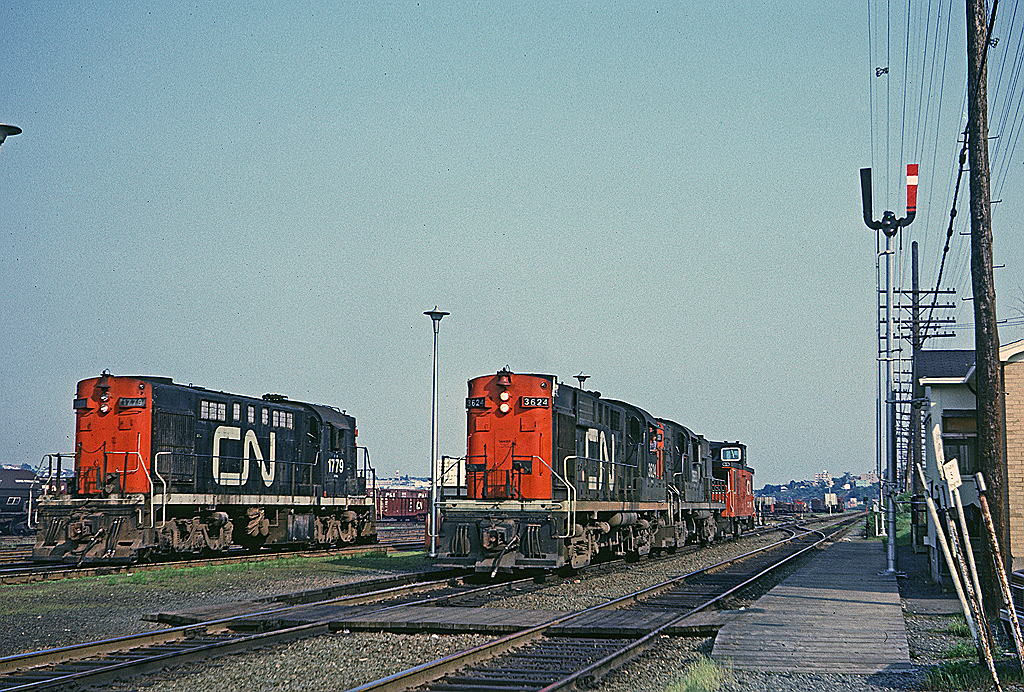 This was an unusual movement. A pair of RS-18s came into Rockingham Yard with a train and then headed west van hop. It was very unusual to see a pair of RS-18s on the road in the Halifax area at this time. 

CN 3624 was wearing a variation of the noodle paint scheme that a few RS-18s and RSC-14s wore - a yellow frame stripe replacing the white (gray) stripe that was standard with that scheme. 

CN 1779 sitting to the left would have been switching Rockingham on day shift and is now idling by the scale house.