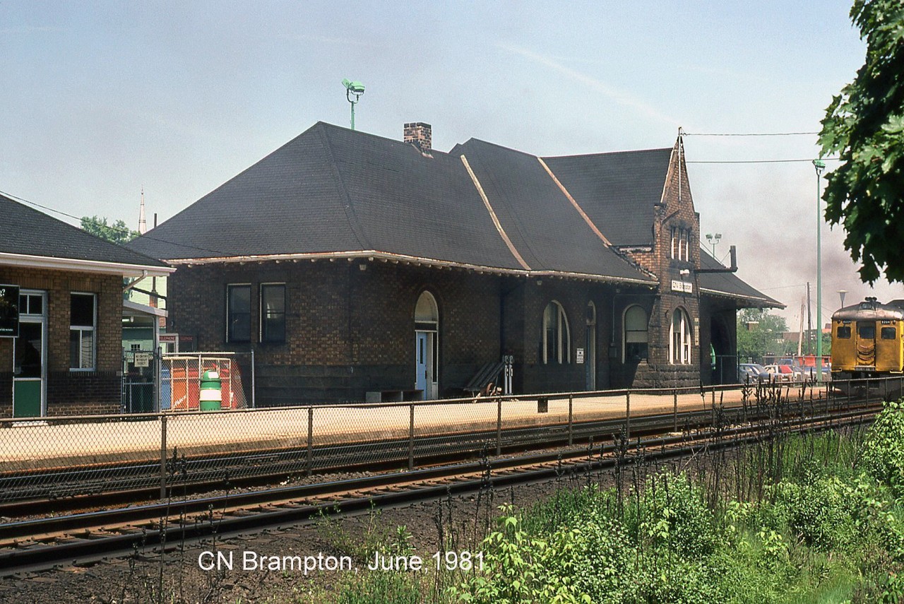 The old GTR/CNR Brampton Station, downtown on a sunny day as a pair of VIA Budd RDC's accelerate eastbound out of the station platforms bound for Toronto.

According to various historical sources, the Grand Trunk Railway built their Toronto-Stratford line through Brampton in 1856, and the arrival of the railway gave rise to more commercial and industrial activity and allowed the town to flourish. The current elegant brick station was built in 1907 by the GTR, after a push by a local town councillor for better train service and a more up-to-date station to replace the original one.

A few "tenant" changes took place over the years: the station was operated by CN until VIA took over their passenger services. GO Transit introduced their new Georgetown Line commuter service in April 1974, originally operating its ticket booth out of the former Express building on the left (note green door and fencing preventing entry without a ticket, before the POP era). Today the station building proper is home to both VIA and GO, still in regular use over 100 years since it was built.