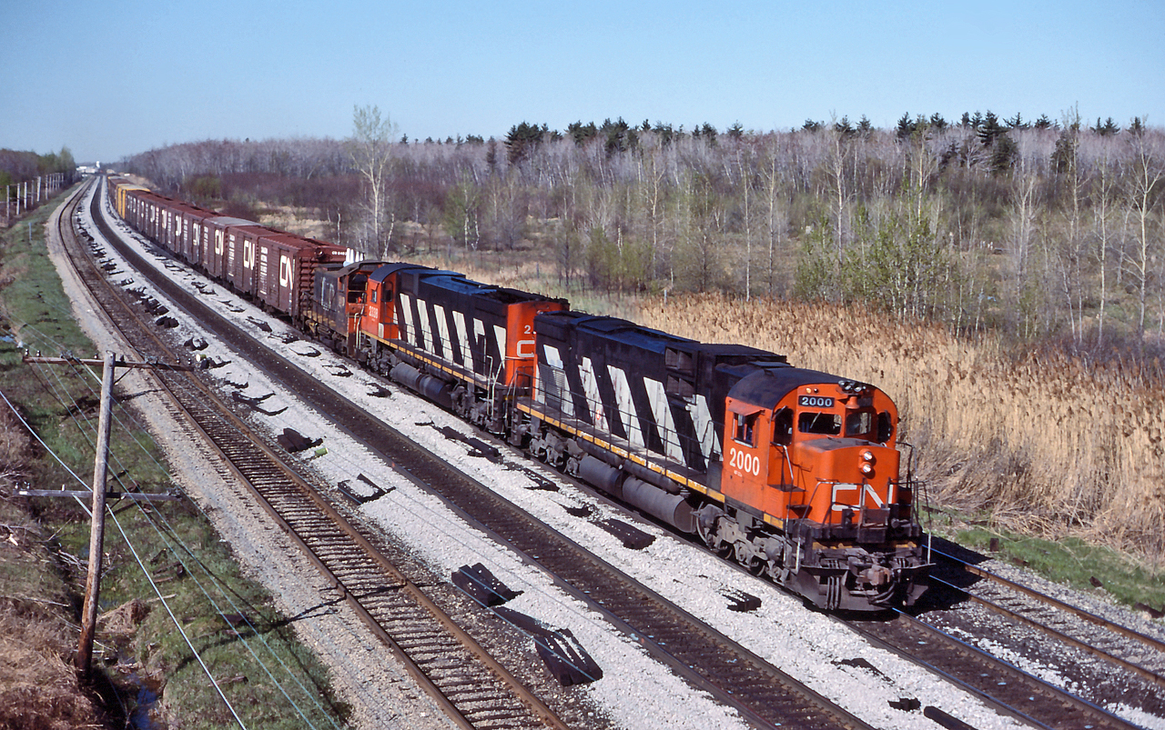 CN 2000, CN 2338 and an unknown SW1200RS leads an eastbound manifest through Les Cedres on the Kingston Sub.