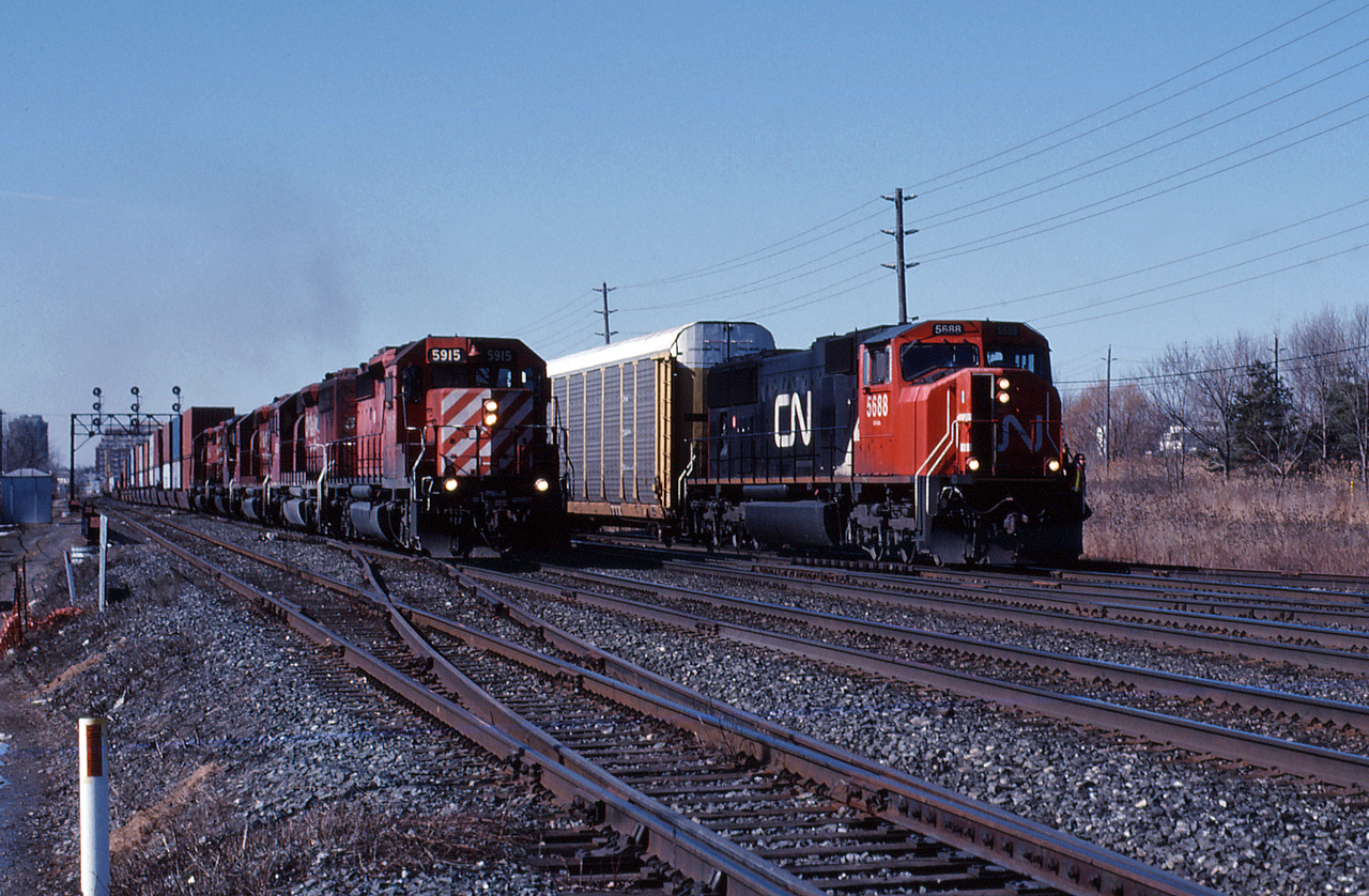 On a quiet Sunday morning, CN 332 with the CN 5688 slows down to enter the yard at Oakville where they will set out some autoracks for the Ford plant before continuing eastwards to Oshawa.  As CN 332 eases through the crossover, CP 153 wastes no time accelerating by on the south track with 5 SD40-2's, making a mile a minute down the high speed Oakville Sub.