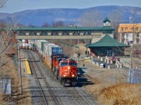 CN 120 heads east through St-Hilaire with a trio of GE products (CN 2234, CN 2204 & CN 2604) pulling a long string of containers bound for Halifax. When it passed one of the horns was stuck in the open position! In the background is the Mont-St-Hilaire Station and parking lot, the end of the line for the AMT Mont-St-Hilaire line.