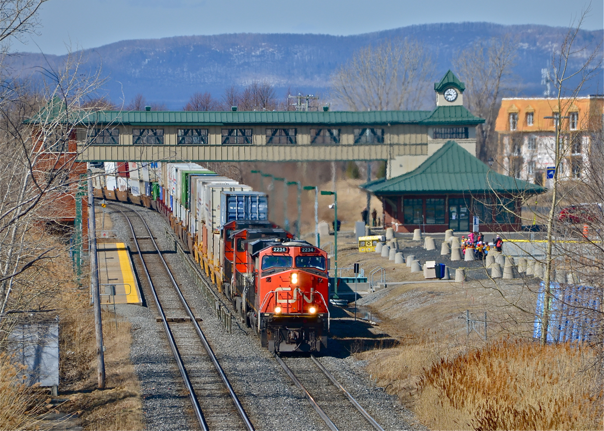 CN 120 heads east through St-Hilaire with a trio of GE products (CN 2234, CN 2204 & CN 2604) pulling a long string of containers bound for Halifax. When it passed one of the horns was stuck in the open position! In the background is the Mont-St-Hilaire Station and parking lot, the end of the line for the AMT Mont-St-Hilaire line.