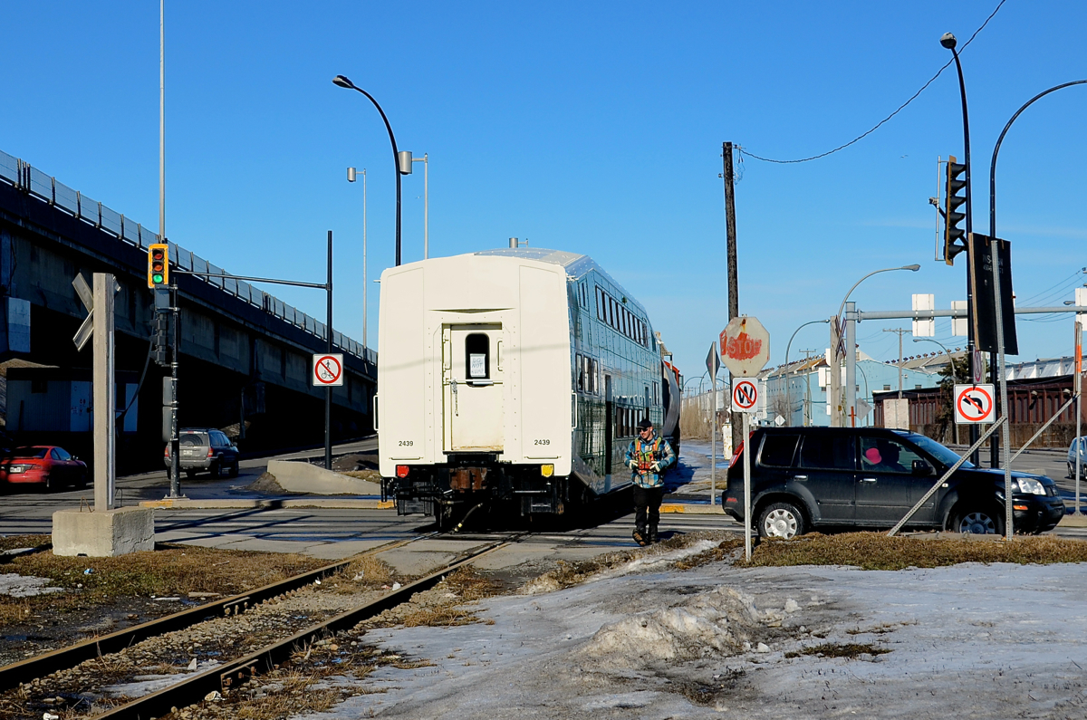GO Transit car through the crossing. GOT 2439 is being pushed to CAD (Canadian Allied Diesel) by CN 7020 & CN 7017 where it will be refurbished. A crewmember is flagging the busy St-Pierre crossing. This spur is no longer in use since a bit over a month now.