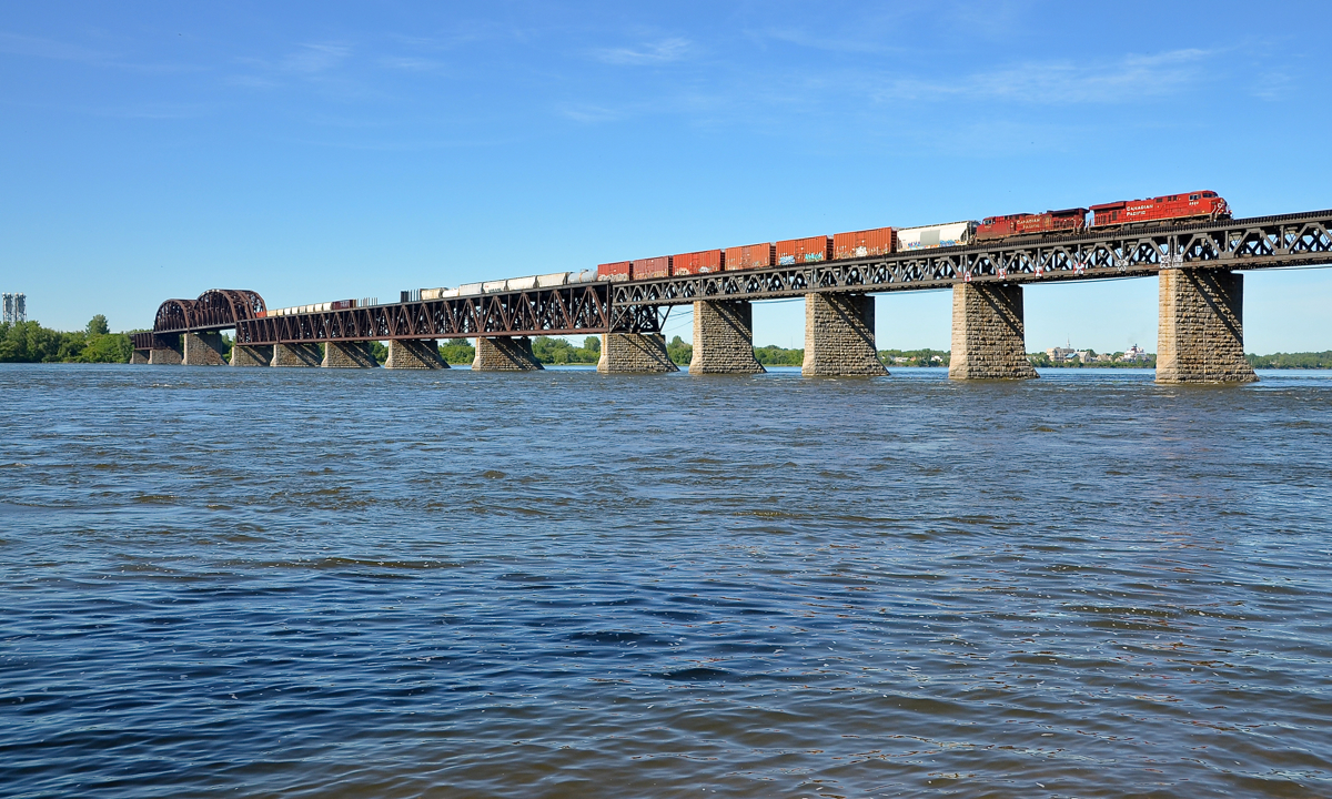 CP 253 crossing the St-Lawrence river. CP 8820 & CP 9804 lead CN 253 over the St-Lawrence river after waiting for the Seaway bridge to go back down after a boat passed. The Seaway bridge is visible in the distance at left.