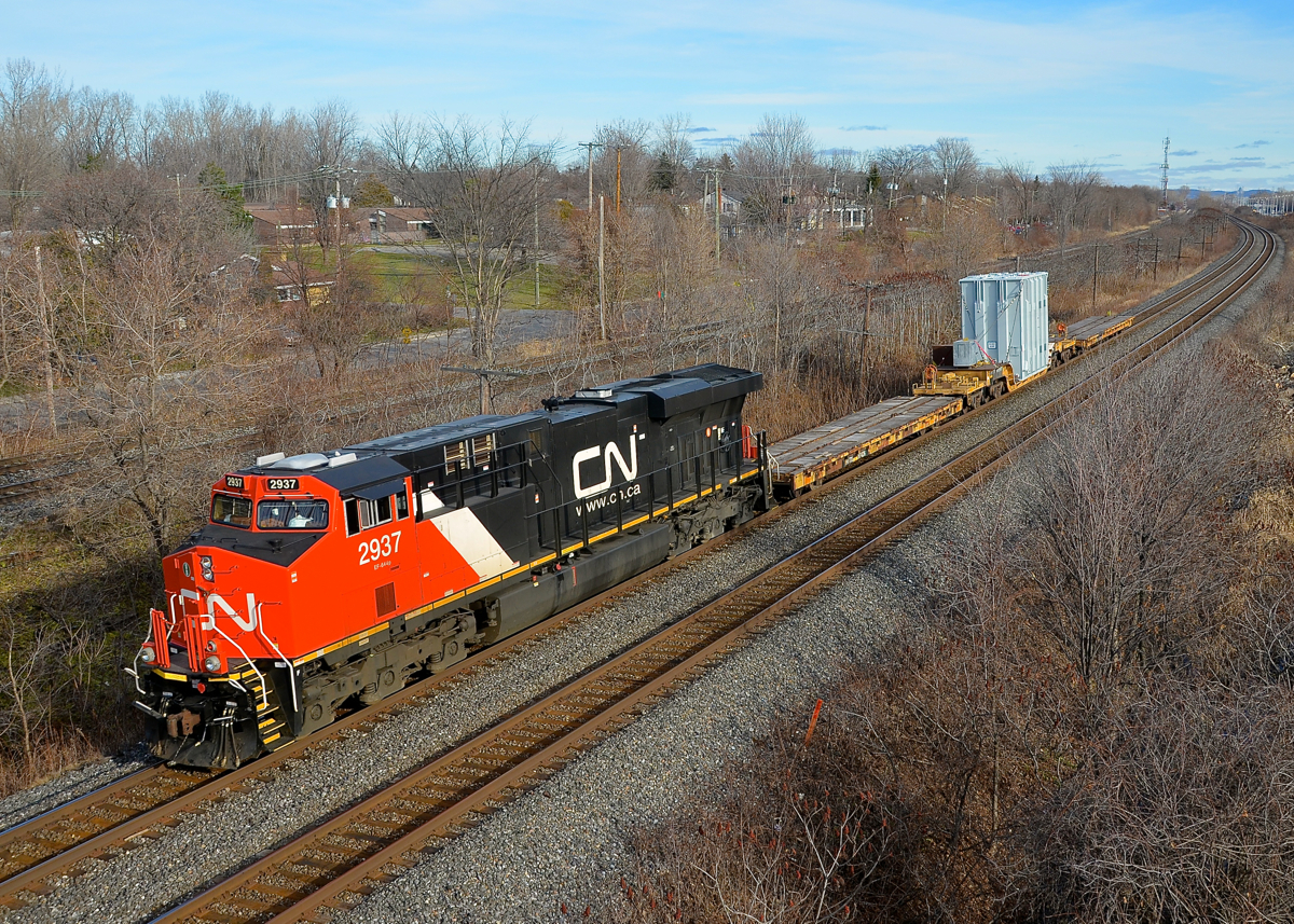 A big and heavy load. CN 2937 has two idler cars and what I believe is a generator on an 8-axle flatcar (QTTX 130561) as it heads west through Beaconsfield. This is CN L351, a dimensional train that does not run very often. The movement is restricted to 25 mph, and the detector at MP 17 of the Kingston sub would indicate the train had 22 axles and was doing 24 mph. The load is bound for Flint, Michigan.