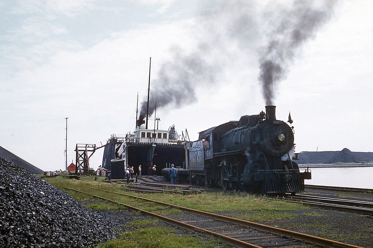 A small group of bystanders has gathered to watch rail cars of coal being unloaded from the car ferry Ashtabula. A common site in the small cottage town on the shores of Lake Erie. Coal arrived from the US to be used at CP facilities across Ontario. The 888 a D10 style locomotive would switch out the loads while the Port Burwell way freight would take the cars north. A lengthy process being that only a dozen cars could be taken at a time to Ostrander where the train would be marshaled together, because of the grades out of Port Burwell.