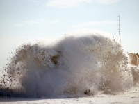 A frozen drift of heavily packed snow explodes as the plow extra north hits it hard at speed. 