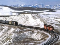 An eastbound manifest approaches the what was Glenbow siding, east of Cochrane. It was a nice clear day and the mountains and local area are covered with fresh snow.  I am not so sure that having 4 empty flat cars right behind the engines is such a good idea, even if the following hoppers are also empty, but I might be wrong.