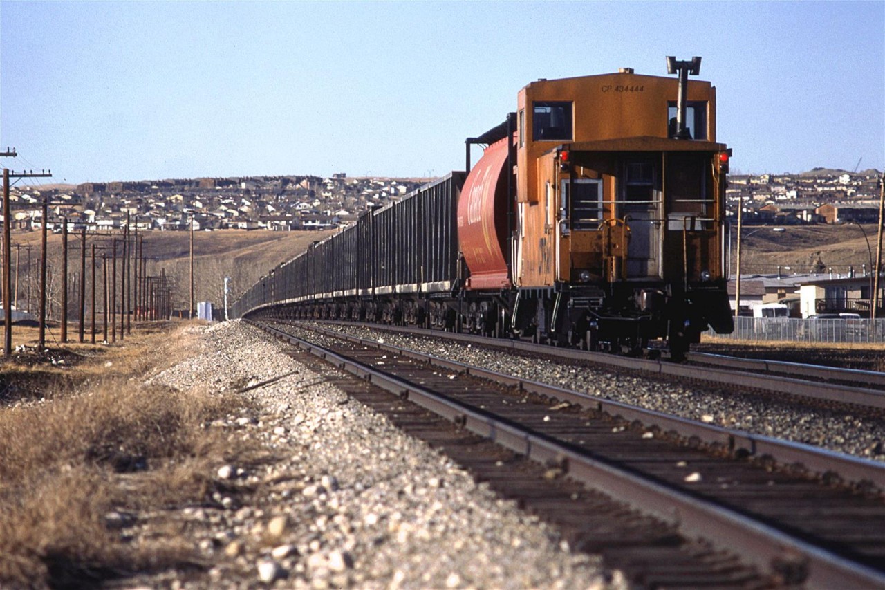 The rear of a sulphur train, with its prerequisite buffer car between the caboose and sulphur cars. It straddles the slight rise at Brickburn in west Calgary on this late afternoon.