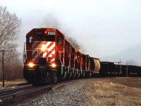This is my last photo taken on March 27, 1986. That haze in the air is in fact smoke from a grass fire on the hill over my right shoulder. After the train passed, I escaped by crossing the tracks and then a footbridge over the Bow River. 
As for the train, it is a westbound manifest at Edworthy Park, in West Calgary. Although it looks like a sulphur train - buffer car and black gondolas, I think that the gon's may be for aggregate, and the grain car may not be placed as a buffer. Presumably, there are other types of cars and cargo on the train out of frame. 