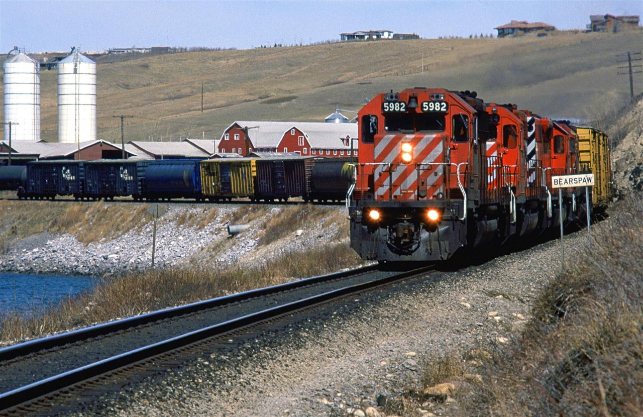 This eastbound manifest is coasting along Bearpaw reservoir in west Calgary. The "Bearpaw" sign indicates that the next location (a siding) is "Bearpaw". I can't be certain, but on the back side of the sign, it might read "Kieth". The attractive barn and farm are still there now.