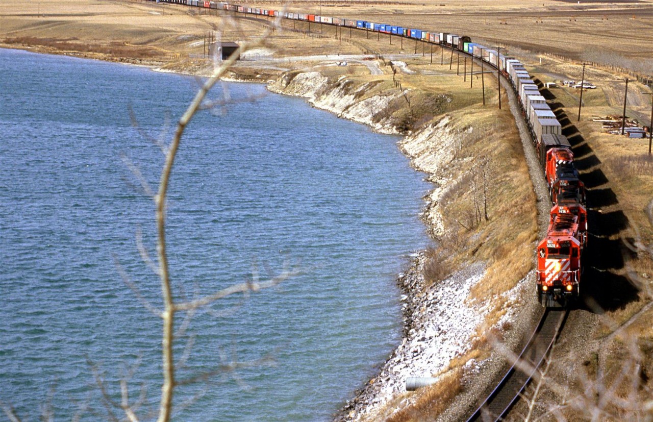 An eastbound intermodal train is on the outskirts of Calgary along the bow river (Bearpaw Reservoir). Given how many obstructions that were there in '86, I suspect that this view is not possible now.