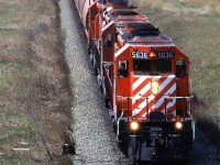 An eastbound empty grain train passes through Kieth yard, in the background. What looks like snow in the background is gravel. There is a large aggregate operation on/in that hill on the horizon.