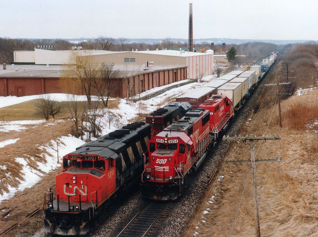 Unless there is some sort of emergency or detour, we will not come across the likes this scene again, for CP no longer runs over the CN Oakville sub in order to get to Toronto. On a typical dull late winter day, CN 5310 and 5087 wait for CP's #557 to pass behind SOO 6054 and CP 780 before proceeding into the Aldershot yard. Of the four units pictured, only the SOO 6054 is active in Canada, now as CP 6254. Photo taken from the Lemonville Road bridge. The stack in the background is a relic of the former Burlington Brick Works, now demolished.