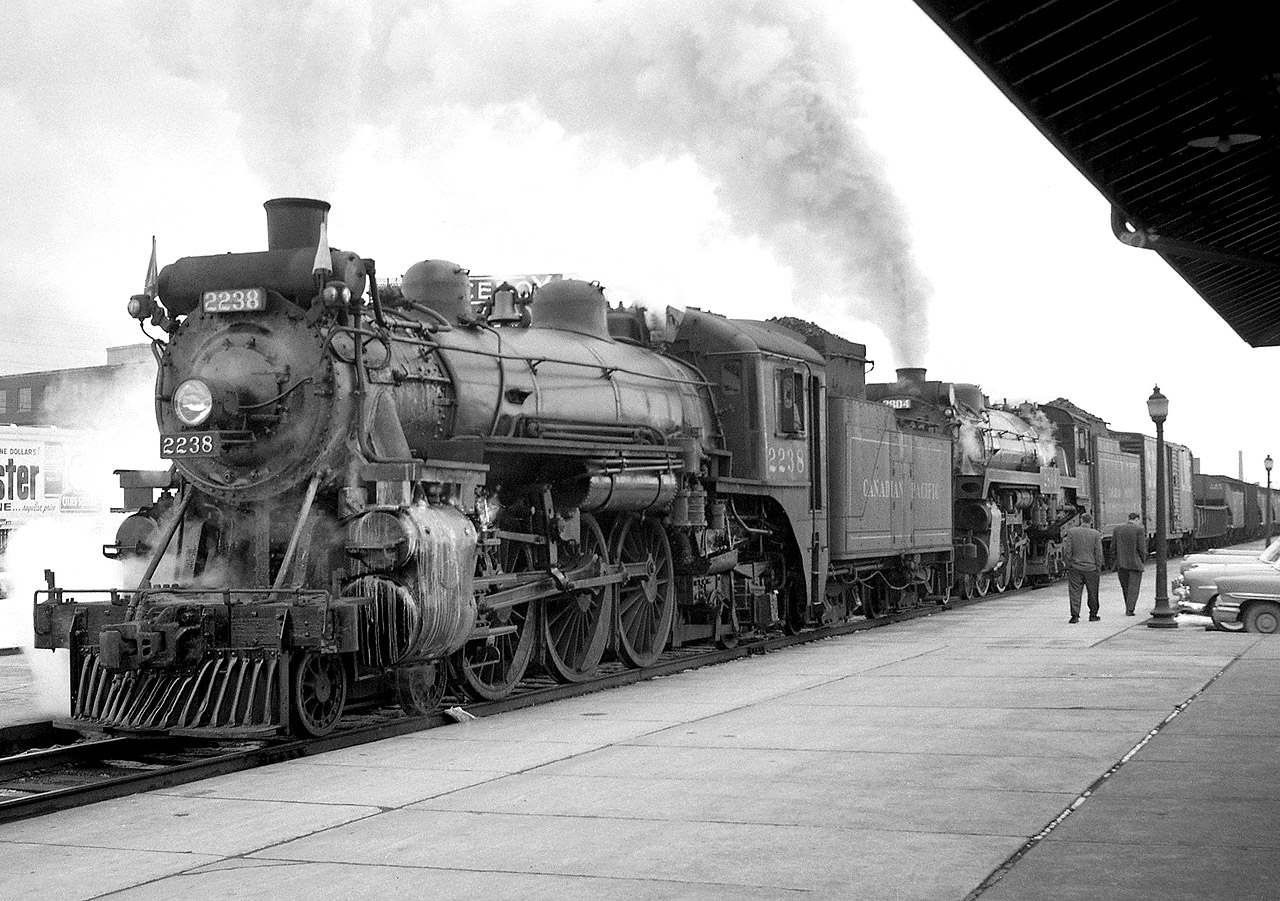 Canadian Pacific Railway G1-class 4-6-2 2238 and H1a-class "Hudson" 4-6-4 2804 wait in front of CP's West Toronto Station for clearance up the MacTier Sub in 1958. Assist engine 2238 (doubleheaded on the front end of the train) will come off at Bolton. The procedure here is the train has backed out of Lambton Yard on the Galt Sub to the station, and will now use the connecting track to cross the diamonds with the CP North Toronto and CN Brampton (Weston) Subs to proceed north up the MacTier Sub.

More CP at West Toronto:
More doubleheading CP steam: http://www.railpictures.ca/?attachment_id=14058
Doubleheading CN Northerns: http://www.railpictures.ca/?attachment_id=19407
CP "Trainmaster" 8917:http://www.railpictures.ca/?attachment_id=15874