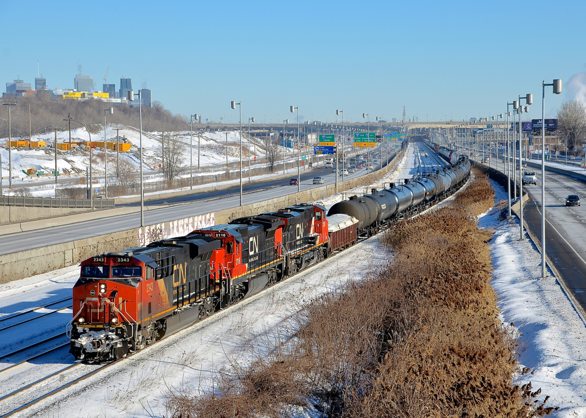 A late-running CN 305. A later than usual CN 305 is slowly approaching Turcot West in Montreal where it will get a new crew. Power is CN 2343, a very clean CN 2116, CN 2258 and DPU IC 2711. CN 2116 & CN 2258 are just along for the ride, as both are on idle. In the background at left is the skyline of downtown Montreal.