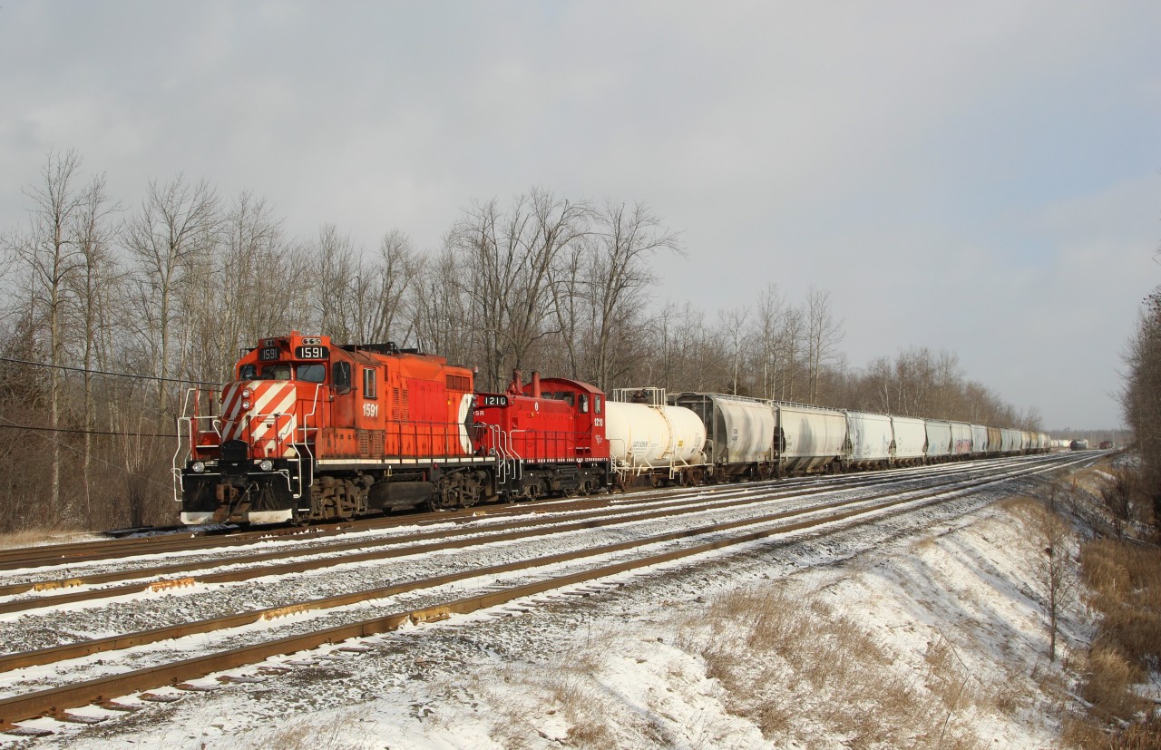 Guelph Junction Railway 1591 (GMD GP9u) along with OSR 1210 (GMD SW1200RSu) are switching hopper cars and tank cars at Guelph Junction as they approach the First Line with a band of snow clouds approaching.