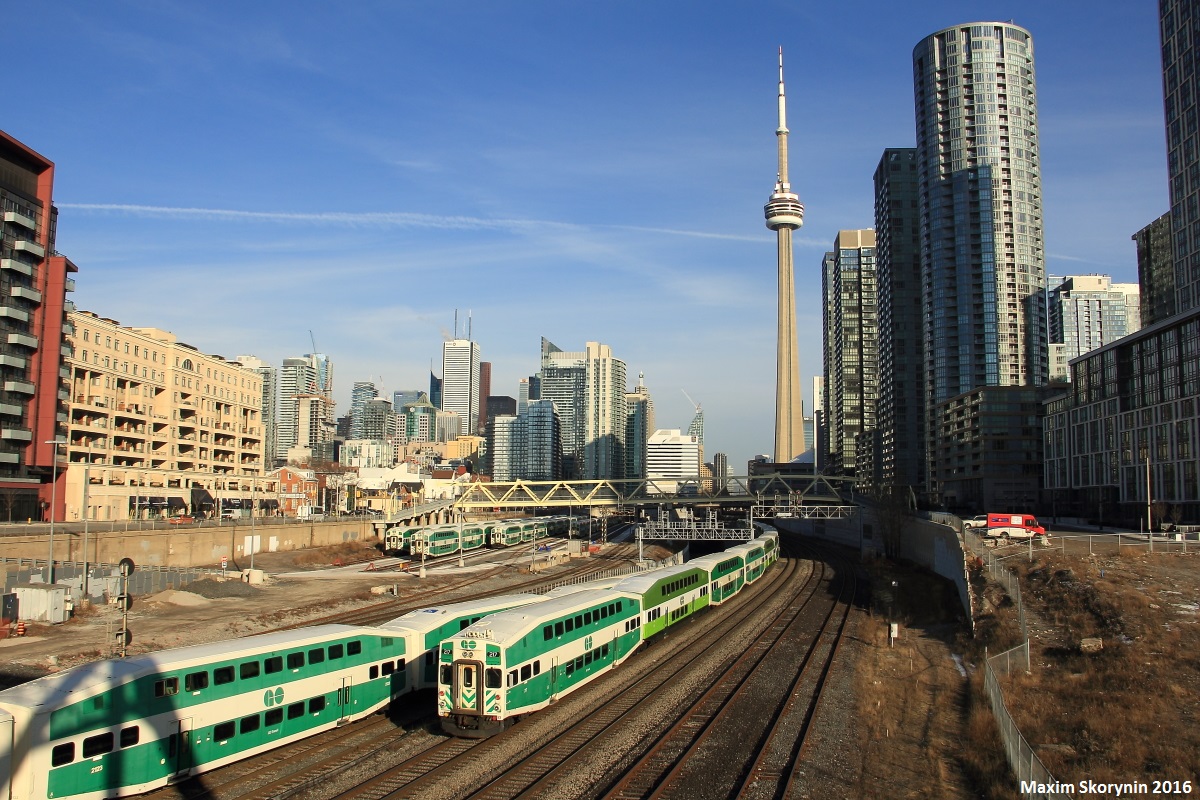 With the Toronto skyline, including the world-famous Canadian National Tower in the background, a westbound GO Transit commuter train heading towards Hamilton exits on this sunny Monday evening, among the other commuter train rush.