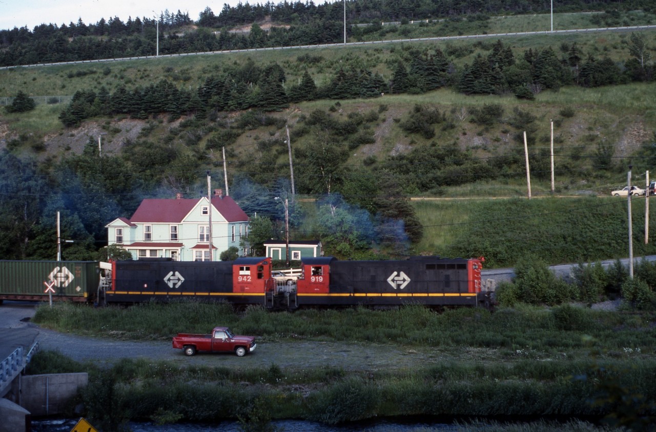 The engineer of NF210 # 919 opens the throttle of Terra Transport Extra 919 West at the Symes Bridge grade crossing in St. John's just before sunset on the evening of July 7, 1988. Built in 1956 by GMD of London, ON, this unit was one of an order of 26 diesels delivered from Montreal to St. John's on the MV Christian Smith to forever banish the Mikado and Pacific steam engines still operating on the narrow gauge line. With less than three full months of operation remaining, the sights and sounds of trains running through the scenic Waterford Valley would end for good on September 30 and the former Newfoundland Railway would be nothing more than a memory.