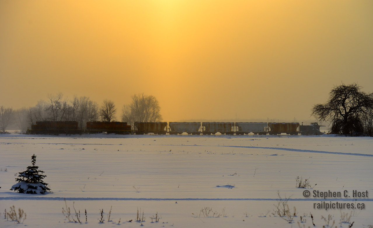 Almost home, Goderich-Exeter's daily Goderich wayfreight is passing eastward by the warm glow of a winter sun, a pillar of orange from ground to sky created by light flurries refracting light in all directions. Framed in a tree, GEXR 55413 brings up the rear as the crew performed the first plow run of the season westward earlier this morning.