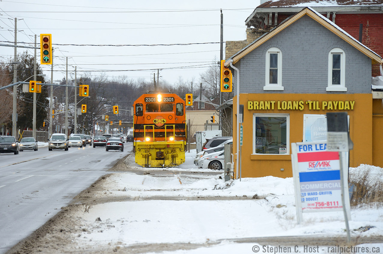 Want a loan? Need a Loan? RLHH 496 trundles along Clarence St past some of Brantfords finest downtown establishments, with green arrows indicating clear signals for both the railway and cars. 

Funny Story, A bit earlier I was with Rob Smith waiting for the train who was discussing with me when 496 would make its appearance. Time kept ticking and lunch was nearly over. Rob said "I have to pull a Mooney and go.. which means as soon as I leave the train will come". Rob left, and sure enough so the train came. How our friend Arnold got wrapped into this is a thing of legend, but I'll let the legend himself comment below to how this Mooney-ism came to be :)
I don't make the trip to Brantford often, only once or twice a year, but I was lucky this day as they were 5 hours late allowing me the chance to catch them during an afternoon off. To me this really is a time machine, being a SOR (RLHH) operation, and having missed the first time RLHH operated this spur from 1997 to 2000 or so.. with just a single customer, this could last for decades, it could last for months, you just never know. Glad to have shot it!