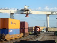 Intermodal train passes under the overhead cranes while a SD40-2 yard engine waits for clearance.