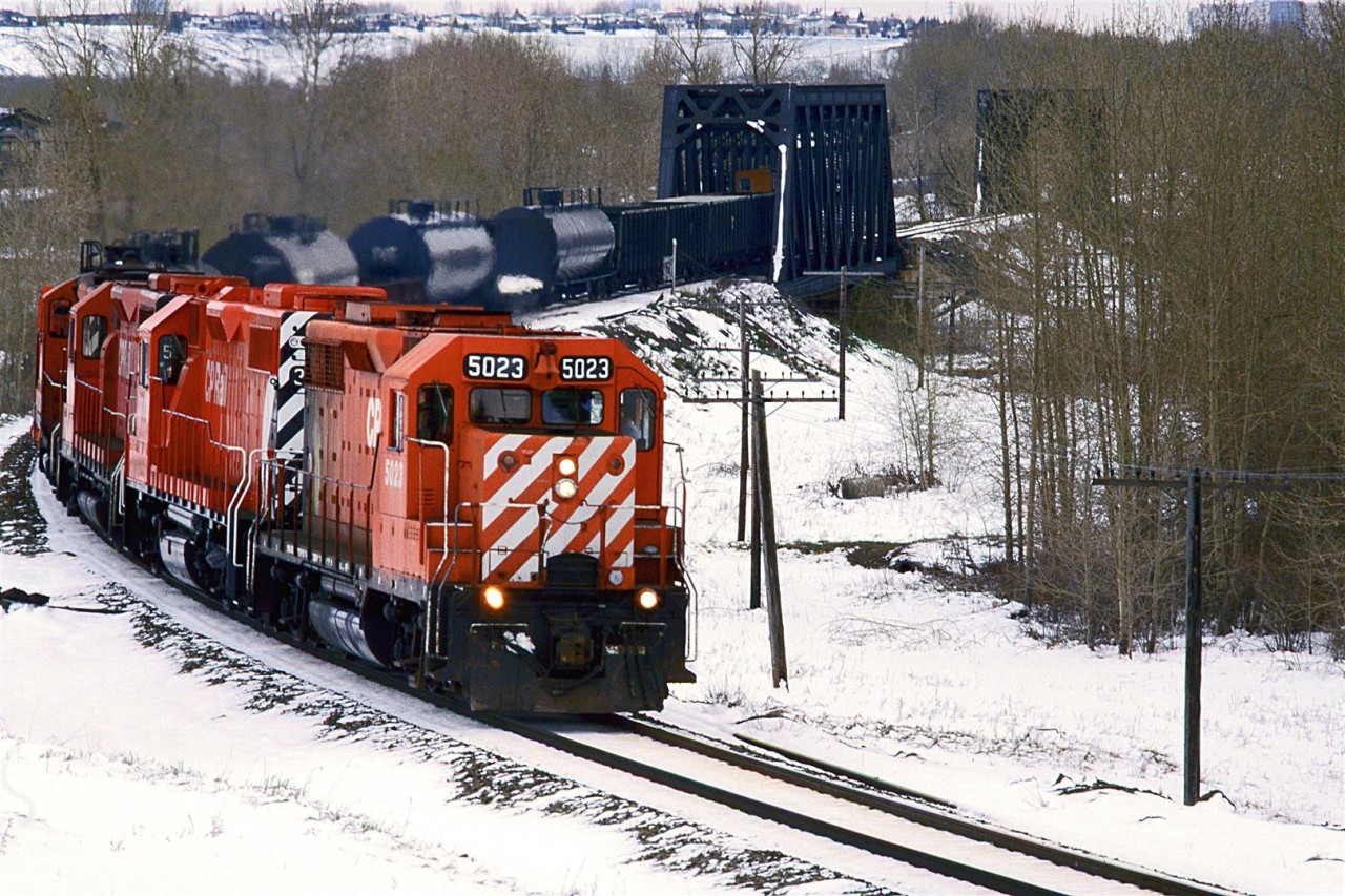 This is interesting. We have a relatively rare GP-35 leading the "Exshaw Turn" this day. Also, it is one of the very few trains operating shortly after this May snow storm. But what I think is the most notable aspect of the photo is the consist. The tank cars are separated by flat cars, suggesting that there is something contained in them that requires special handling - perhaps explosives for the quarrying at Exshaw?
There are several empty aggregate cars in behind the tank cars. 
Once again, I wish I had taken better notice of things back in 1986.