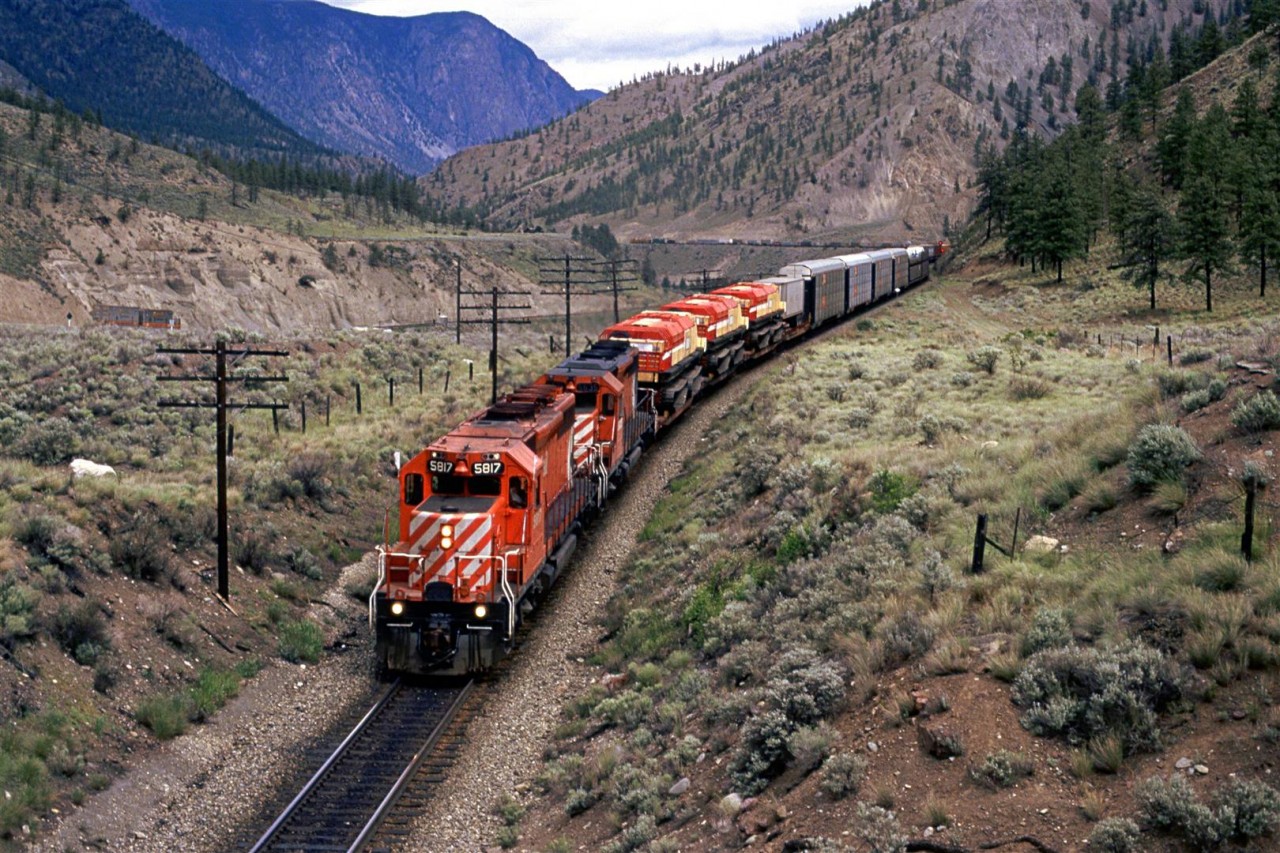 Westbound manifest about to pass under the Trans Canada Highway. The three leading flat cars have interesting tracked vehicles.