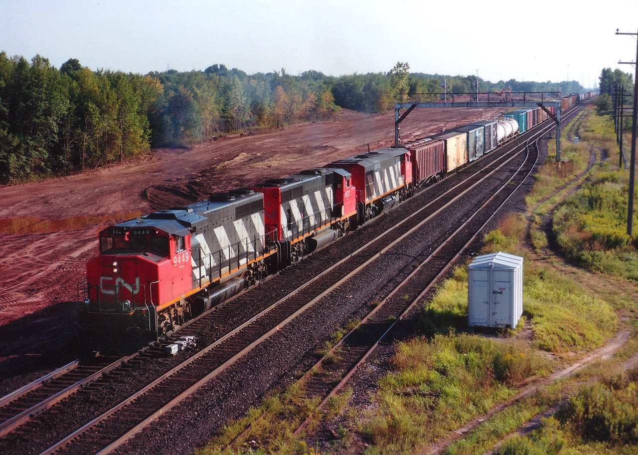 This image was shot from the Waterdown Rd bridge, looking east; in 1989. In view is CN 9449, 9572 and 2112 with train #393. I posted this for a couple of reasons. One being to show the lush green stand of trees in the background; a piece of rural countryside within the City of Burlington. And secondly, in case someone out there wants to match this location with a current image to show for TIME MACHINE. This is an easy opportunity. For behind the motive power, that beautiful stand of trees was leveled for the Aldershot GO station. Those of you out there that believe man is responsible for global warming; why look farther than here? Coolness of the woods exchanged for a hot asphalt parking lot.