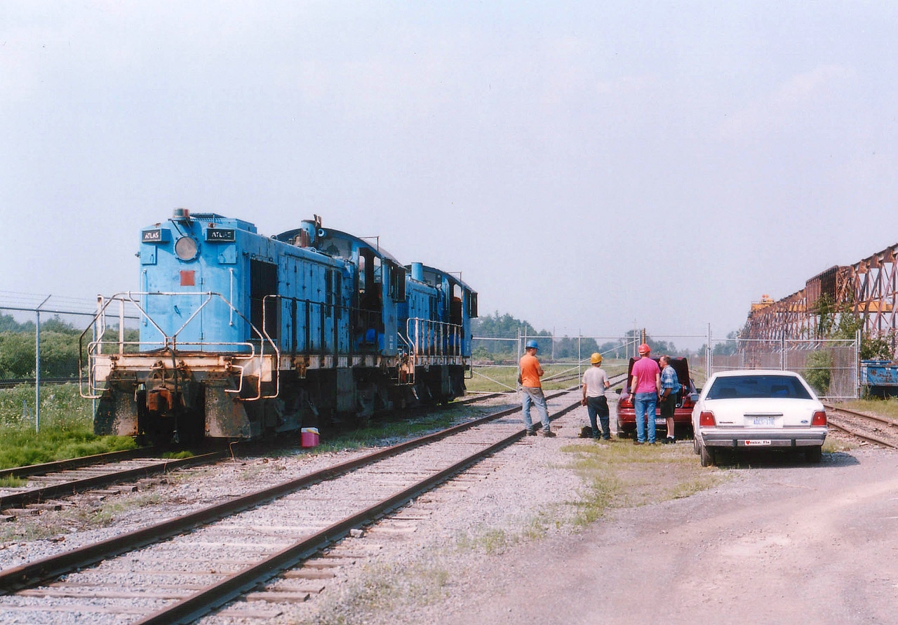 I was sitting at home one hot summer night, minding my own business (I think), and I get this phone call. The "boys" from the Leatherstocking Chapter of the National Railway Historical Society had made it to Welland from Oneonta, NY in quest of a couple of locomotives for the society's tourist train. So, being a member, I am obliged to help out, or at least greet them upon arrival :o). And off I go down to the former Intermetco factory just off the Hwy 406 by the canal. I brought a cooler of water and some other interesting thirst quenchers. It was HOT. So, after a sequence of photos both for myself, for the lads, and the Chapter Newsletter; we got to cleaning out these neglected units.
Slater Steel had purchased Atlas Specialty Steel recently and did away with the plant switchers. The two pictured are x-CN S-7 8223; now Atlas #10 and soon to be CACV 3152. Behind it is x-CN S-4 8181, now Atlas #9 and soon to be CACV 3151. CACV is Cooperstown and Charlotte Valley; the tourist road, owned by the LRHS, based out of Milford, NY.  First thing we stenciled the locomotives "CACX" on account we are not a common carrier railroad, so the reporting marks have to end in the letter "X"; thus making our official interchange reporting marks CACX. Before heading Stateside, both brake systems had to be updated in order to receive a current Blue Card, as required by the FRA. On July 4th Trillium S-13 #110 fetched the units to interchange with the CP for the trip to Cooperstown Jct., NY. They were a long time getting there, but currently both these units are still operating on the railroad. Cooperstown, for the Baseball Hall of Fame, is a great place to visit, and now you know there is a train ride to be had as well. The white car pictured is mine. I actually forgot how I got in there. :o)
