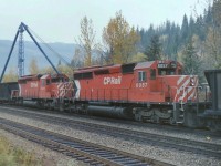 CP mid train units 6048 & 6057 were passing through Revelstoke BC on a typical rainy day in the mountains. The blue crane in the background was used to unload railway delivered products for the new "Revelstoke Dam" which was under construction at the date of the photograph. The photograph was taken from the edge of street. 