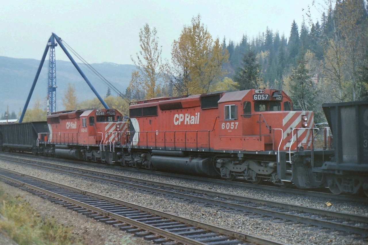 CP mid train units 6048 & 6057 were passing through Revelstoke BC on a typical rainy day in the mountains. The blue crane in the background was used to unload railway delivered products for the new "Revelstoke Dam" which was under construction at the date of the photograph. The photograph was taken from the edge of street.
