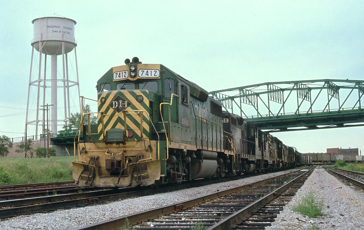 I uploaded an image of this train quite a while back; however, this angle, showing the old Niagara water tower and the Central Av bridge also shows a lot more of the train. Norfolk & Western was involved in a contract dispute that dragged on for a year and a half before a strike was called by the Brotherhood of Railway and Airline Clerks (BRAC). Pickets succeeded in slowing down operations, but the real damage was when secondary pickets disrupted operations of connecting roads. The strike spread, and eventually a month after this photo was taken, over 350,000 employees nation-wide were off the job. The government had to step in. Unfortunately for me, I had planned a cross-USA trip that year. So I remember the Great Strike of 1978. The only trains I saw moving the whole trip were probably operated by non-union company officials and the like. This train, avoiding hassles, crossed Sou Ontario via the CASO. Power is D&H 7412, N&W 830, 2493, D&H 7420, N&W 2709,xxxx, and 1572.