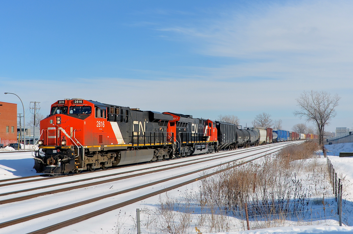 White snow and blue skies. The day after a storm dropped 15 cm of snow on Montreal, covered it with rain and then froze it, the sky is blue and the frozen snow really makes everything brighter as a very late CN 369 heads west through Dorval with CN 2816 & CN 3017 at the head end. Operating mid-train is CN 3018