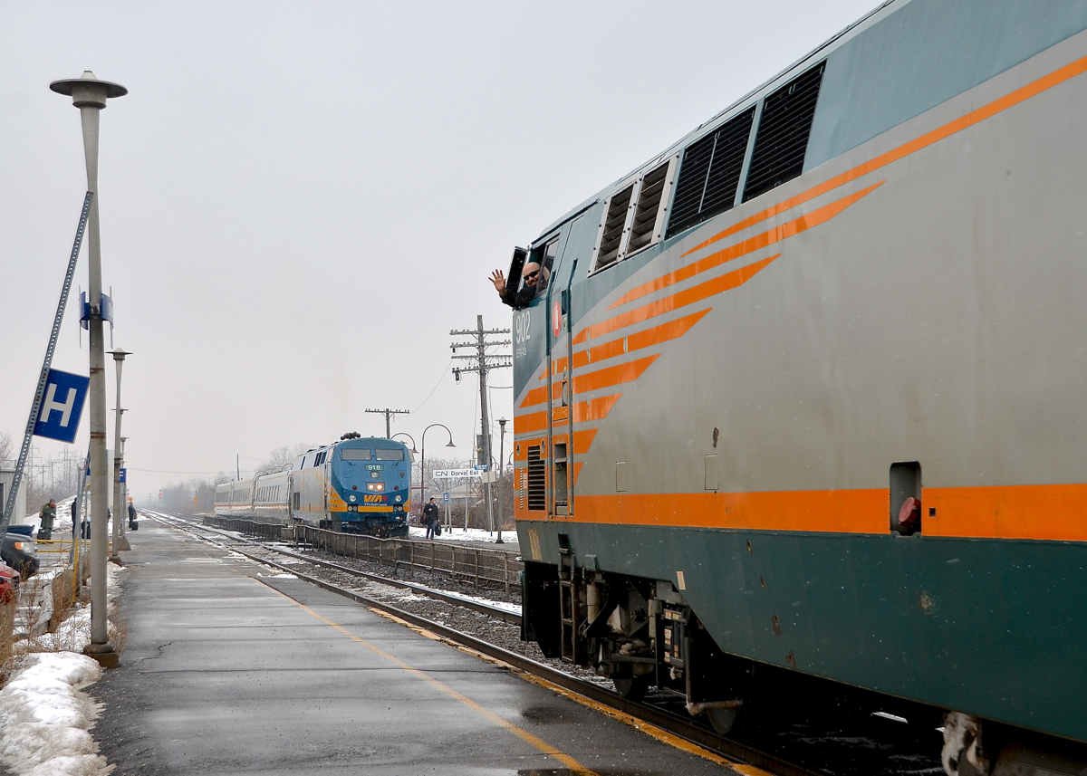 A wave and a P42DC meet. In the background VIA 50 is making its station stop on the north track at Dorval with P42DC VIA 918 leading. At the same time VIA 55 is arriving on the south track with VIA 902 leading as the one of the engineers waves from the cab.