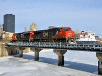 <b>CN 149 and 3 ship funnels.</b> CN 2826 & CN 3038 lead CN 149 over the frozen entrance to the Lachine canal on a cold but bright morning. In the distance the funnels of three ships are visible, laying over for the winter in Montreal. From closest to furthest, they are the <i>Tim S. Dool</i>, the <i>Baie St-Paul</i> and the <i>Algoma Navigator</i>.