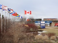CN train 384 with a colourful BC Rail leader passes the colourful arrangement of provincial flags at Chris Hadfield park in Milton.