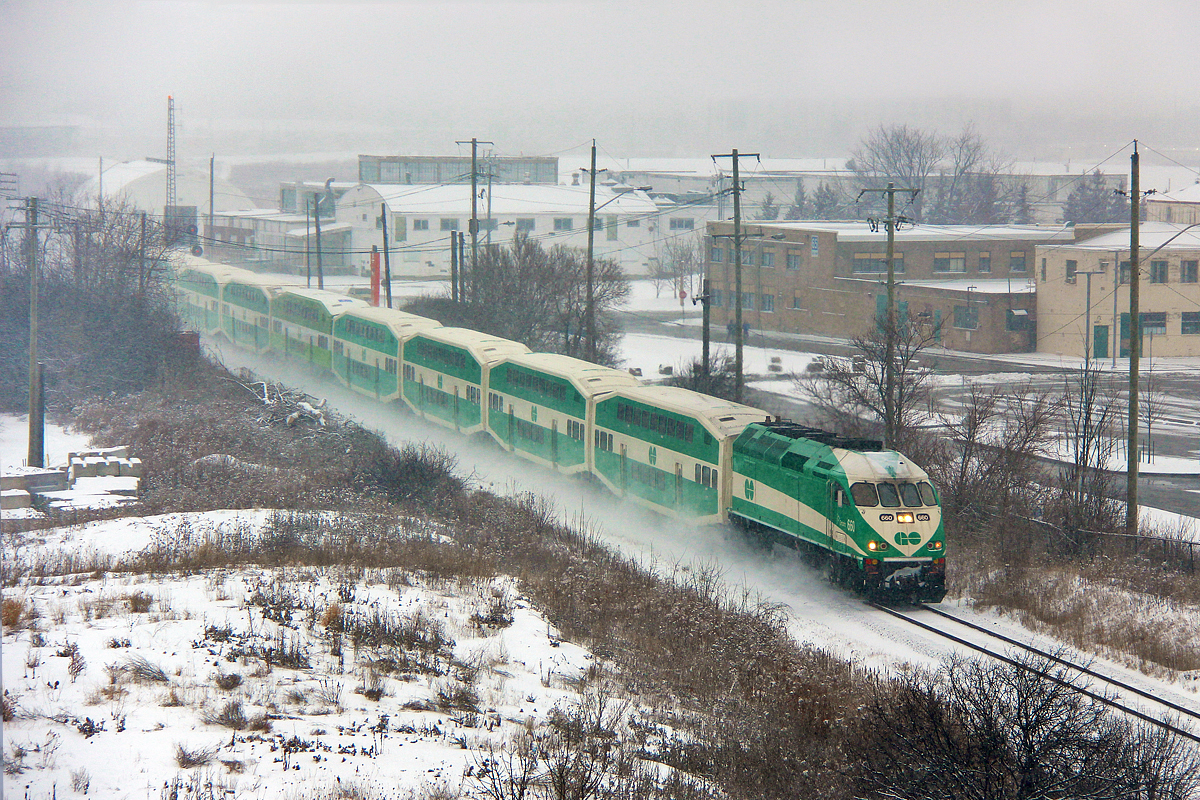 The last southbound GO train from Barrie has just left York University GO station and has reached the track speed of 75mph in no time thanks to a downhill grade. The former CFB Downsview base stands in the background, which is now owned by Bombardier for testing. A morning snow storm is just tapering off, however visibility is still relatively poor. Despite how easily GO tends to be affected by inclement weather, this train is making good time.