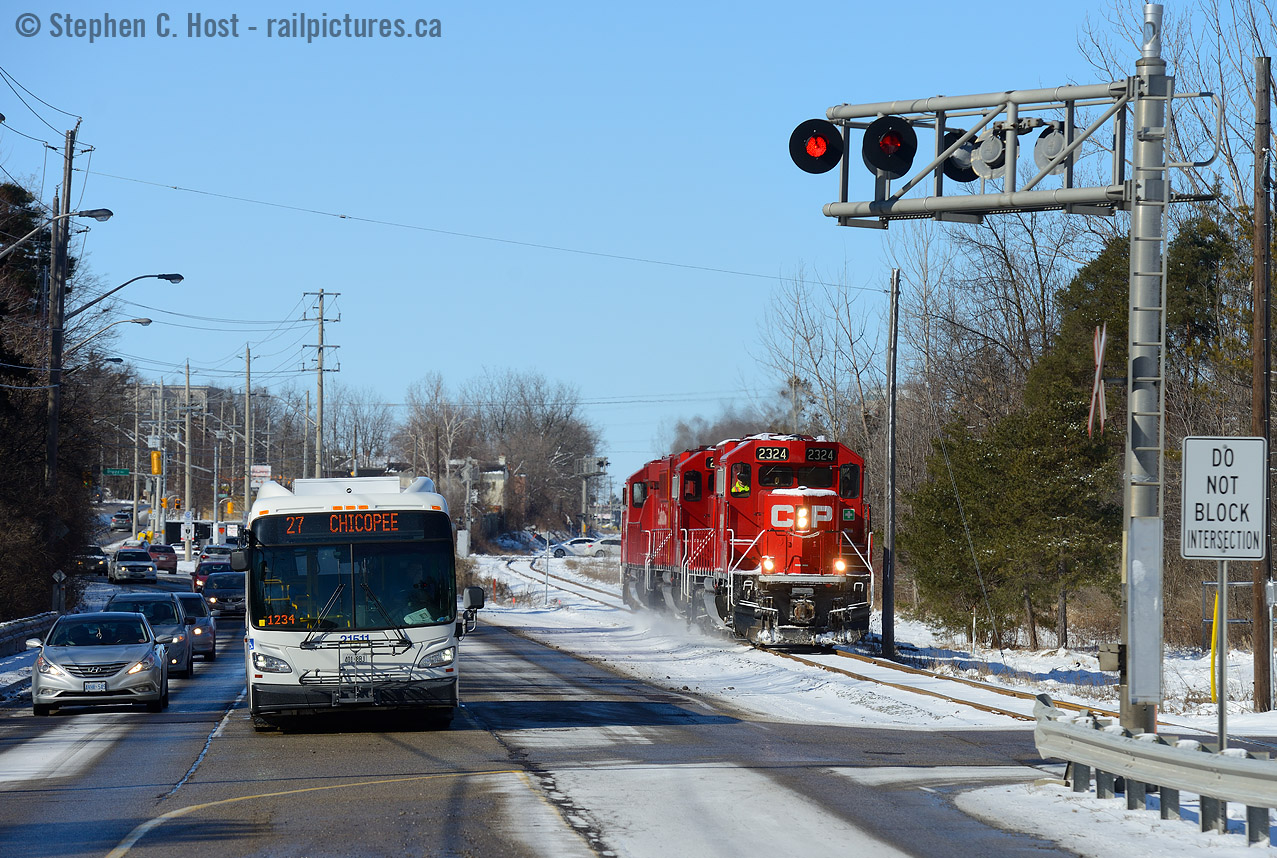 Photo two - the first in this series is T99 northbound at Preston photographed 20 minutes earlier
The Grand River Railway was built to convey passengers and freight, and yet, A Grand River Transit bus, which is the eventual successor of the Motorcars that plied the line now waits for a southbound freight, requiring me to get crafty to get an angle in between the busy King St traffic.
The Waterloo sub is easily good for 100 freight cars a day, not only does the Hagey job work three shifts per day, Wolverton to Hagey turns run 6 days a week in daytime, and sometimes at night to bring cars to this busy line - mostly for Toyota Cambridge assembly. This means two trains are on the line fairly often - under OCS control f.y.i.
Waterloo Region is busy building the ION Streetcar route duplicating the efforts of the GRR (and the former Kitchener-Waterloo Railways Streetcar system) and if phase two happens as planned, this picture will change significantly in the next 10 years, ION is planned to use the CPR route to get down to Galt. Hence, in due time, the Grand River Railway may  again become a busy freight and passenger carrying railway.. stay tuned.