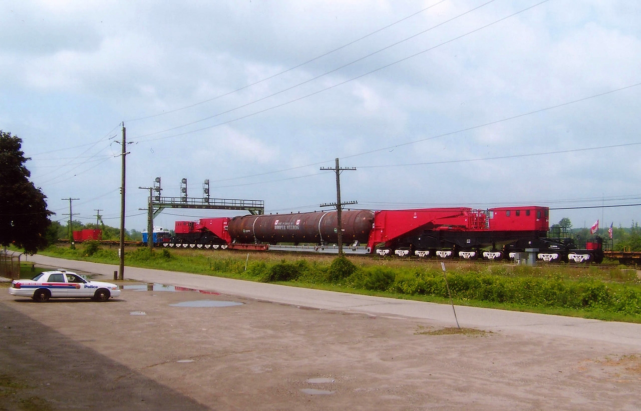 The world's largest rail car, the 740,000 pound Schnabel CEBX-800, with a load consisting of a 675 ton reactor; waits out traffic at Paris Jct before proceeding west on a week long trip to Kansas. This thing is huge; 36 axles; and over 2 million pounds with this payload. CN train #560, with CN 5528 the sole power is on its second day from Oakville, and was to be in London during the overnight. Security was present all along the move, (note the cruiser) although I was able to get permission for some photos from up on rail property of trains passing alongside this monstrous beast. I liked this photo because it gives a good idea of just how big this railcar is.