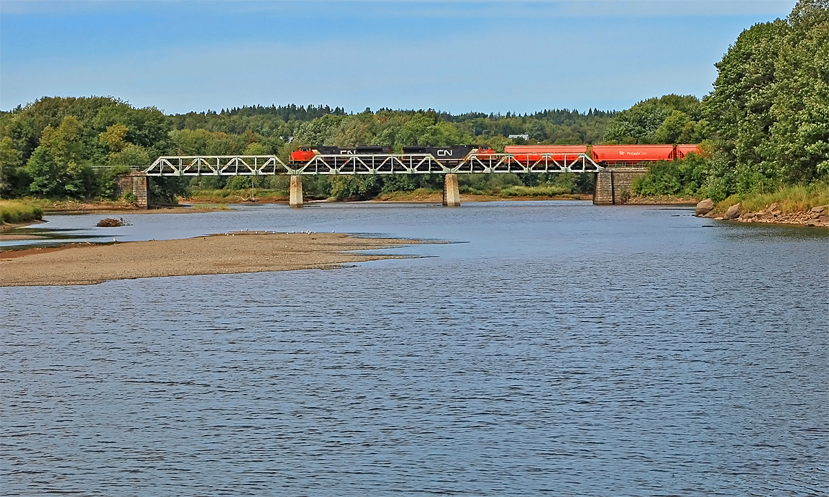 CN 406 with a long string of Potash Corp. hoppers up front glides across the Hammond River heading for St. John.
