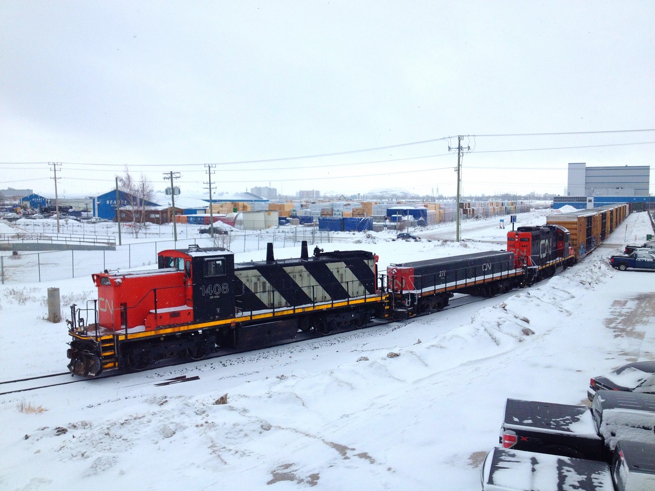CN 1408, 278, and 7239 bring a string of cars across Chevrier Blvd in the Fort Garry Industrial, as they start to round a curve. They are currently carrying 7 boxcars and 6 centerbeam flatbeds. CN 1408 is a rare GMD1, built in 1960.